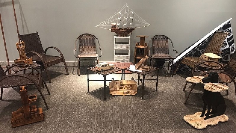 a foto mostra uma sala com paredes brancas e piso de carpete marrom com objetos de madeira, tais como cadeiras, mesas e objetos de decoração.