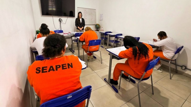 Pessoas privadas de liberdade em sala de aula realizando prova.