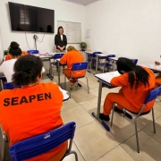 Pessoas privadas de liberdade em sala de aula realizando prova.